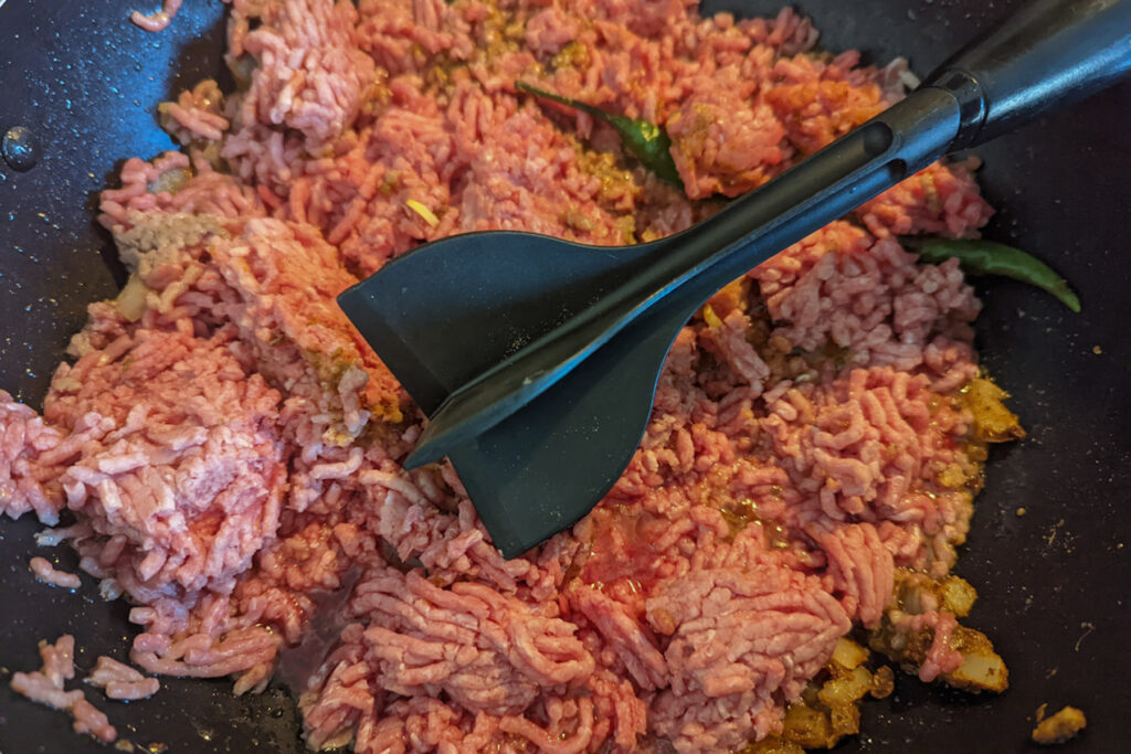 A tool breaking up the ground beef.