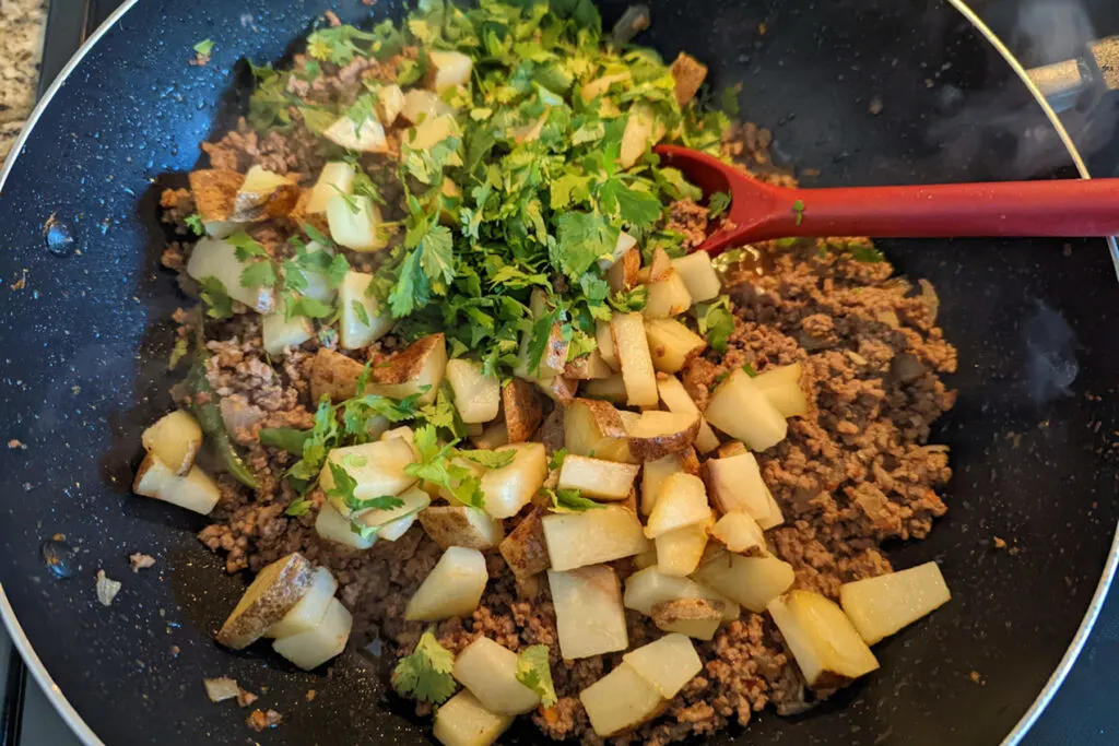 Potatoes and cilantro adding to the cooking ground beef.