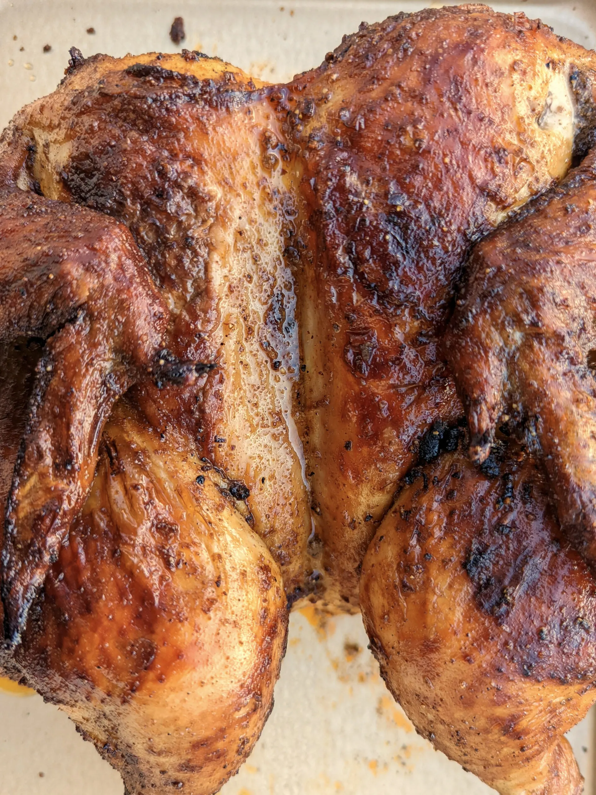 A whole roasted Peruvian chicken on a rimmed baking sheet.