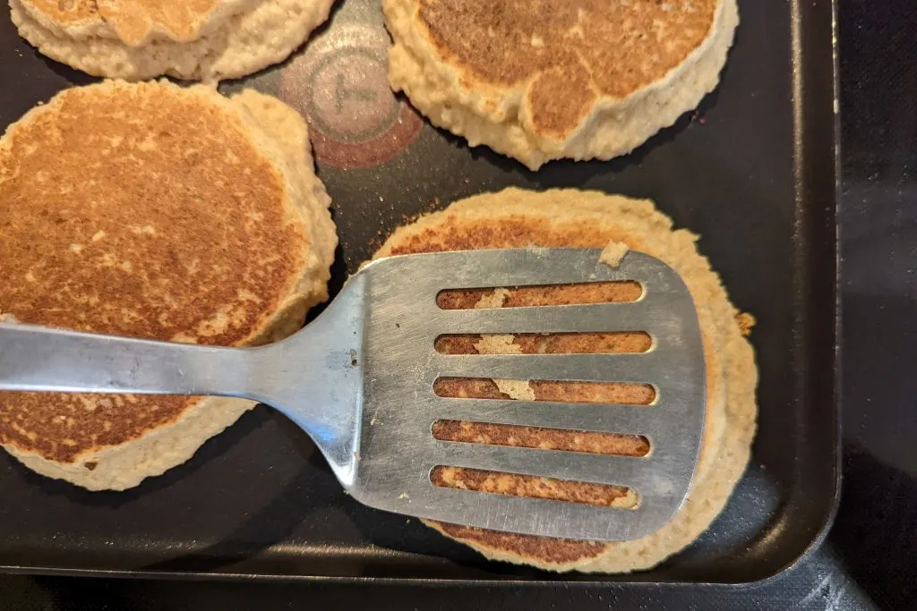 Flipped almond flour pancakes are given a light tap from spatula to spread mixture.