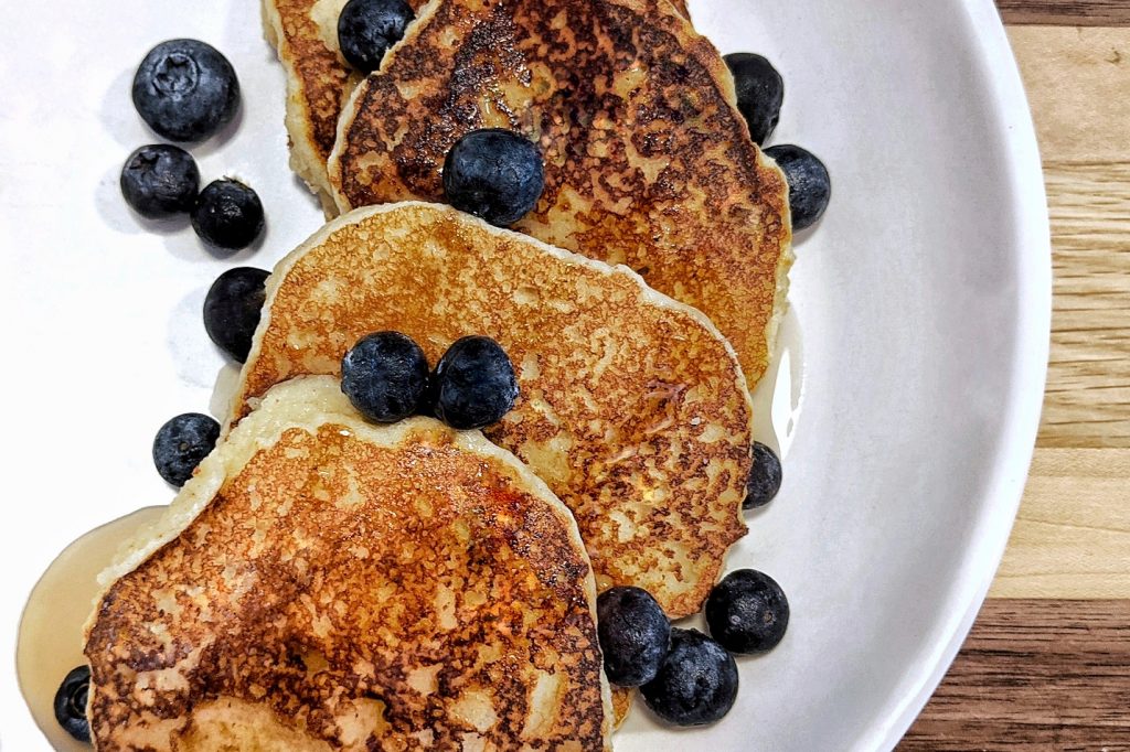 A serving of almond flour pancakes topped with blueberries and maple syrup.