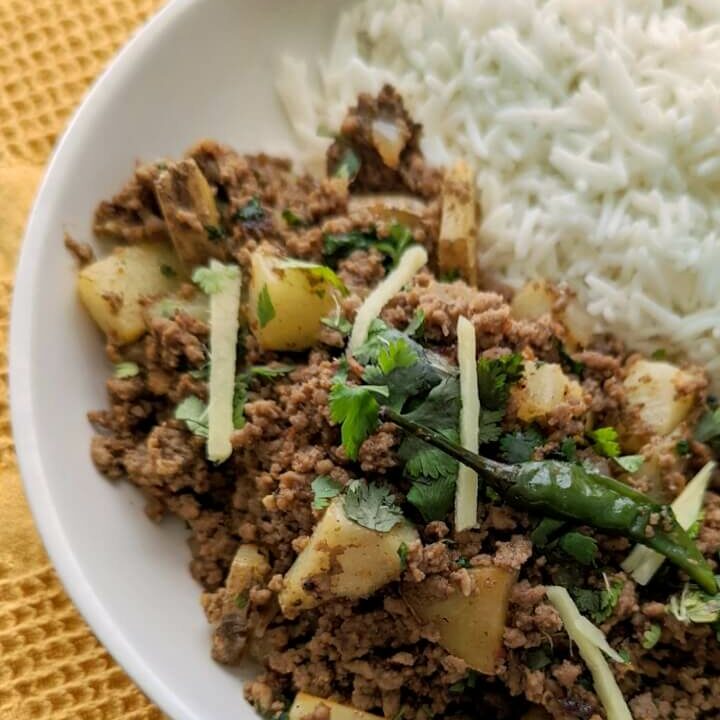 A single serving of aloo keema with basmati rice and garnished with cilantro and ginger.