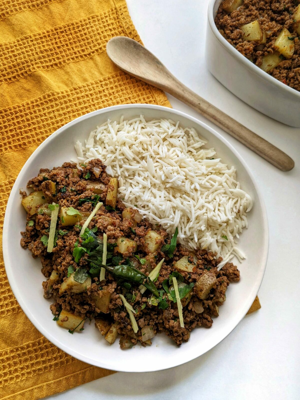 A single serving of aloo keema with basmati rice and garnished with cilantro and ginger.