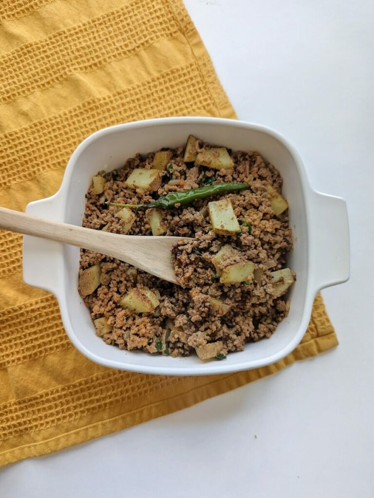 A serving dish of aloo keema garnished with cilantro and ginger.