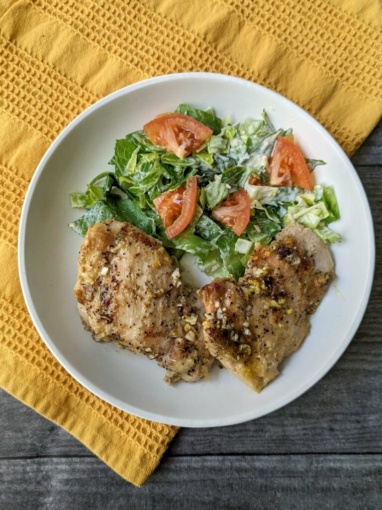 Baked chicken with salmoriglio sauce served alongside a house caesar salad.