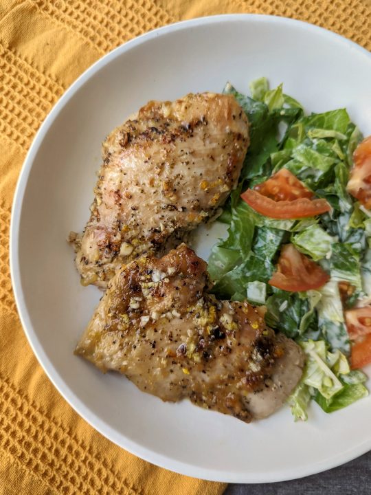 Baked chicken with salmoriglio sauce served alongside a house caesar salad.