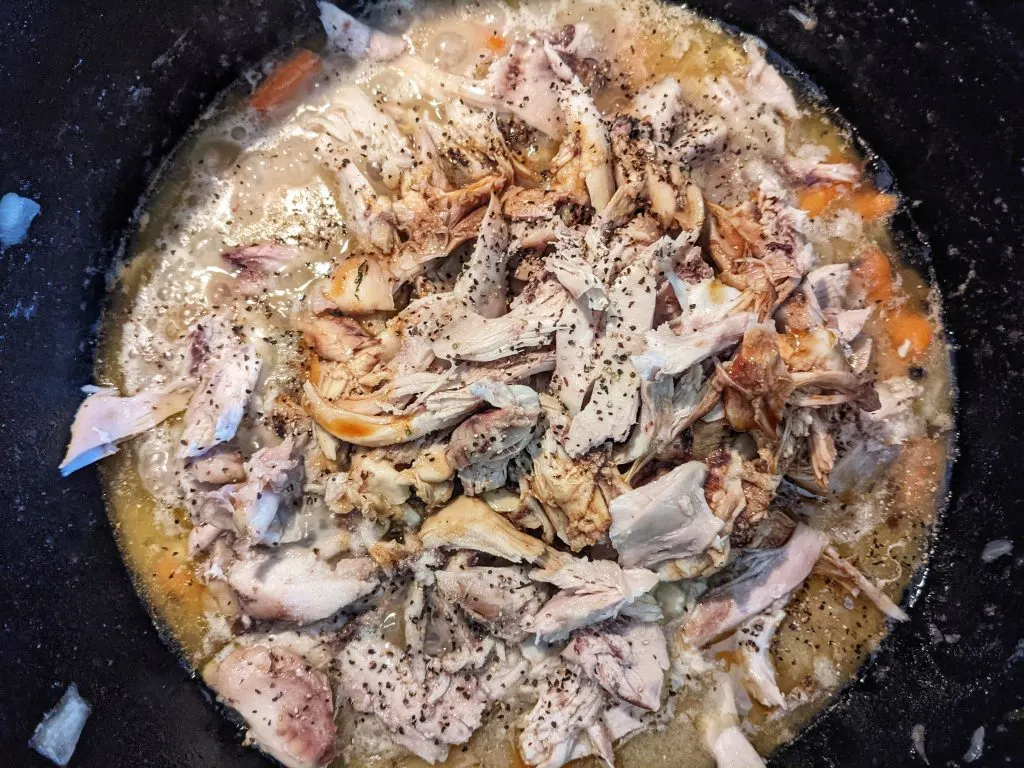 Shredded chicken being added back to the soup.