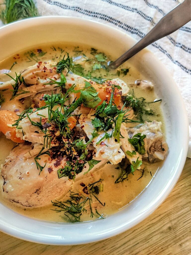 A single serving of homemade chicken soup garnished with red chili flakes, dill, and cilantro..