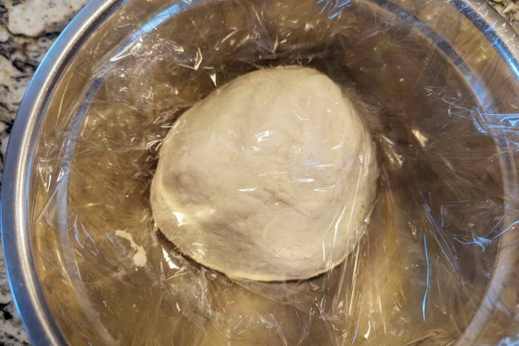A dough ball wrapped in plastic inside of a mixing bowl.