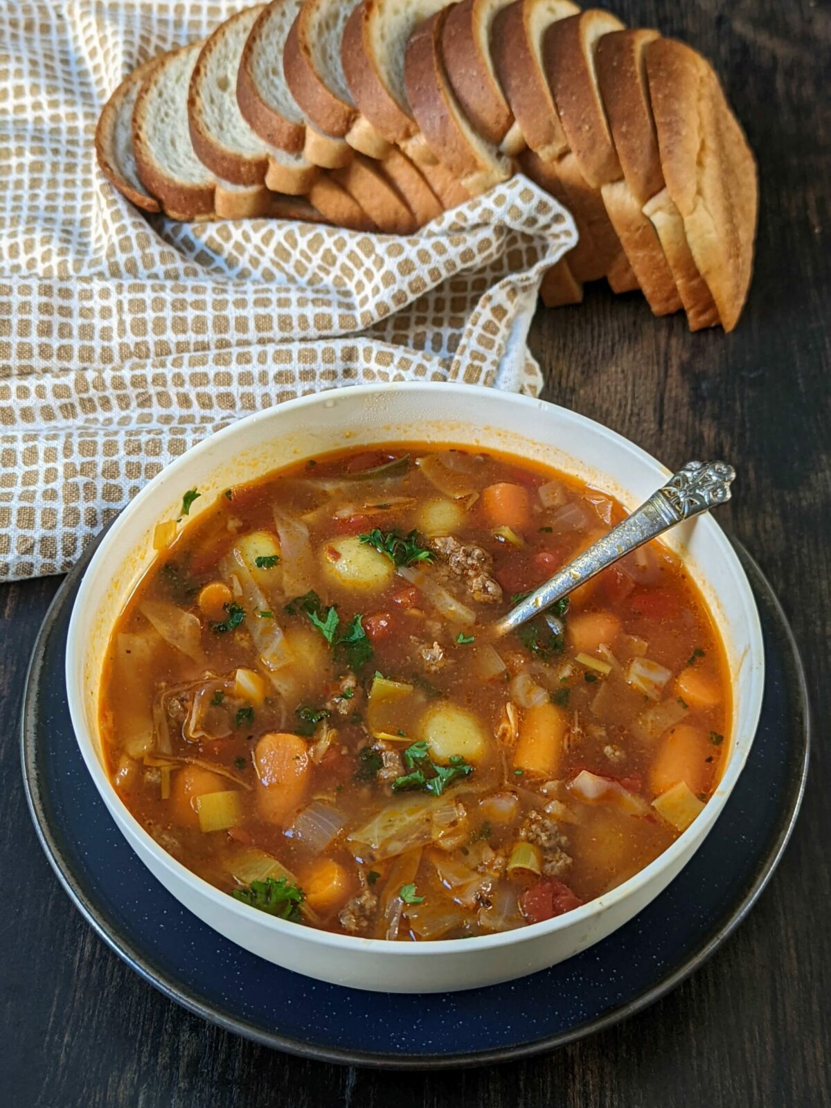 An overhead shot of a bowl of vegetable beef soup with a bread loaf in the background.