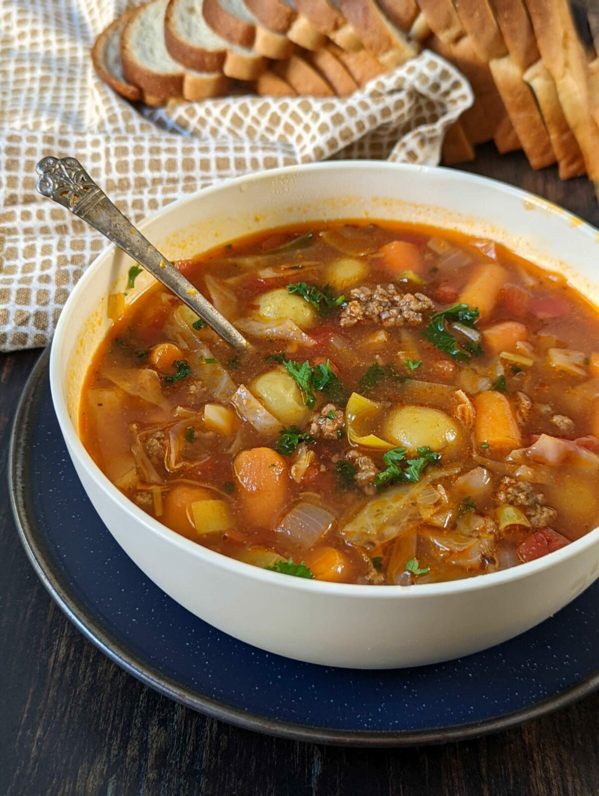 An overhead shot of a bowl of vegetable beef soup with a bread loaf in the background.
