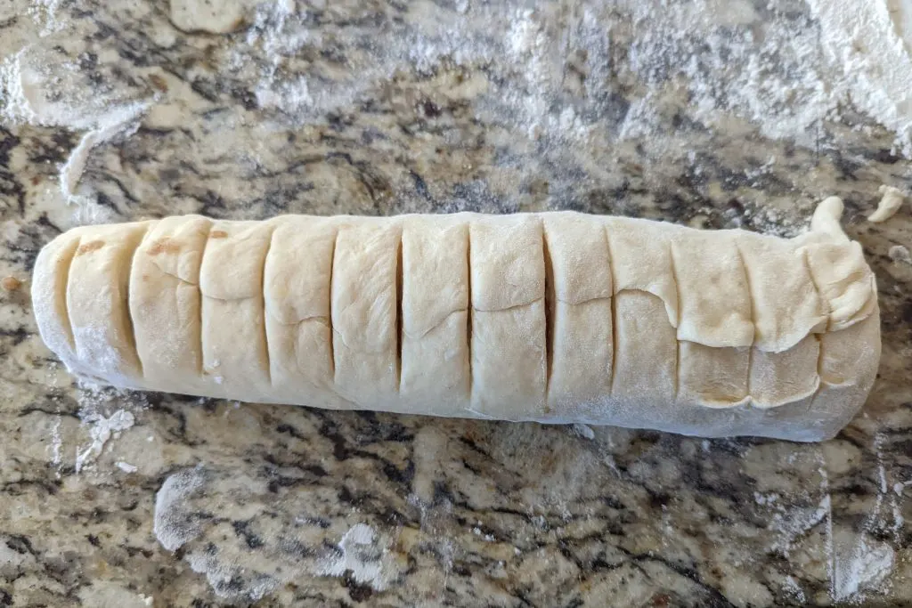 The dough rolled into a cylinder and scored with a knife.