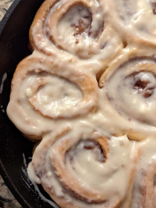 Baked and frosted cinnamon rolls in a cast-iron skillet.