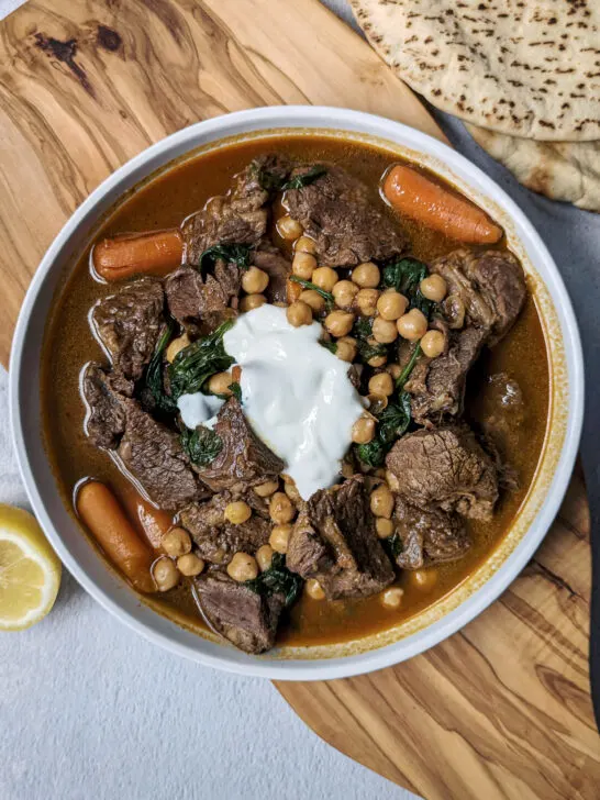 A single serving of beef and chickpea stew topped with yogurt and served with pita and lemon.