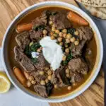 Beef and chickpeas stew in a serving bowl next to pita.