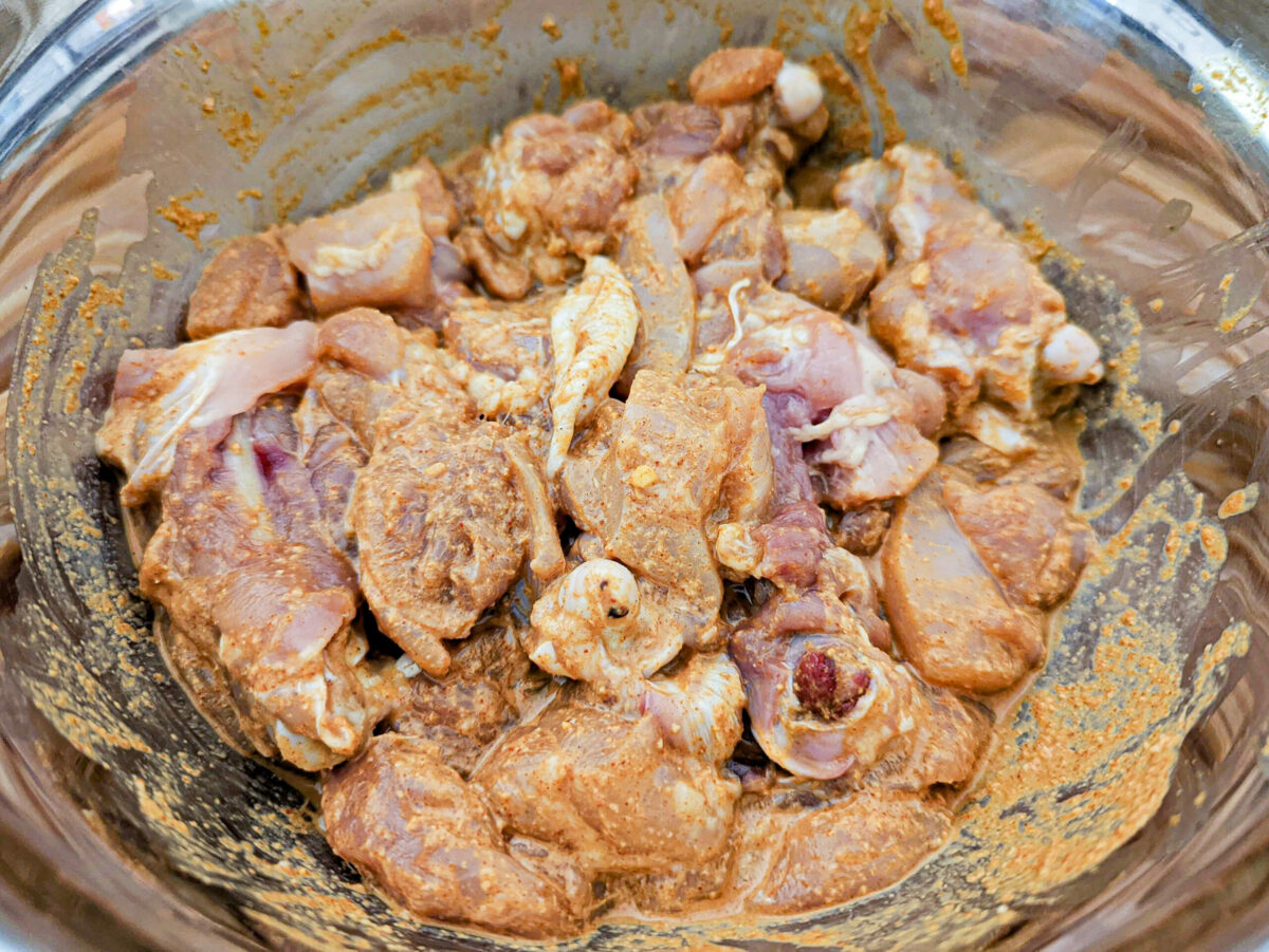 Chicken in a mixing bowl with marinade.