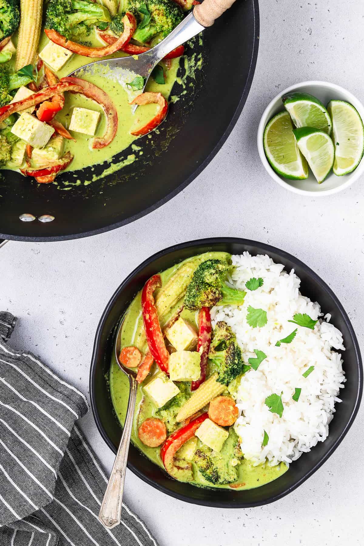 Green thai curry served with rice and lime wedges.