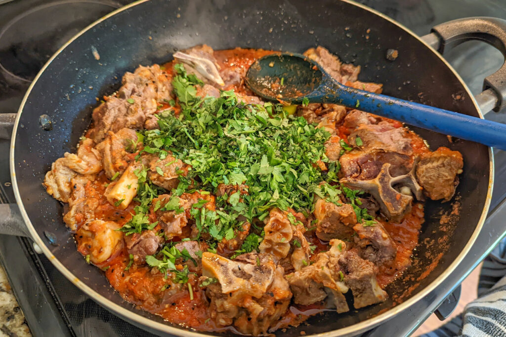 Goat and cilantro added to tomato curry in a pan.