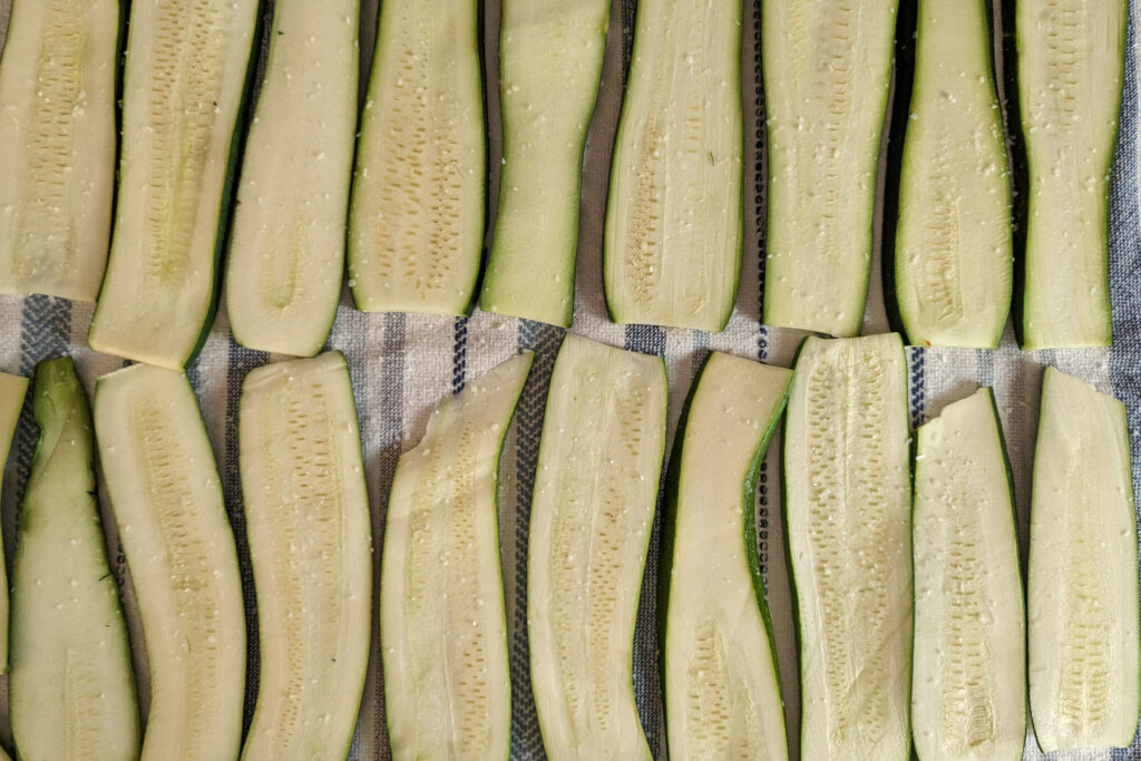 Zucchini strips salted and lined up on a towel.