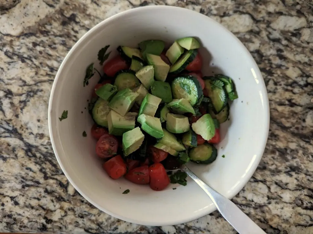 A bowl with the avocado added to the tomatoes and cucumber.