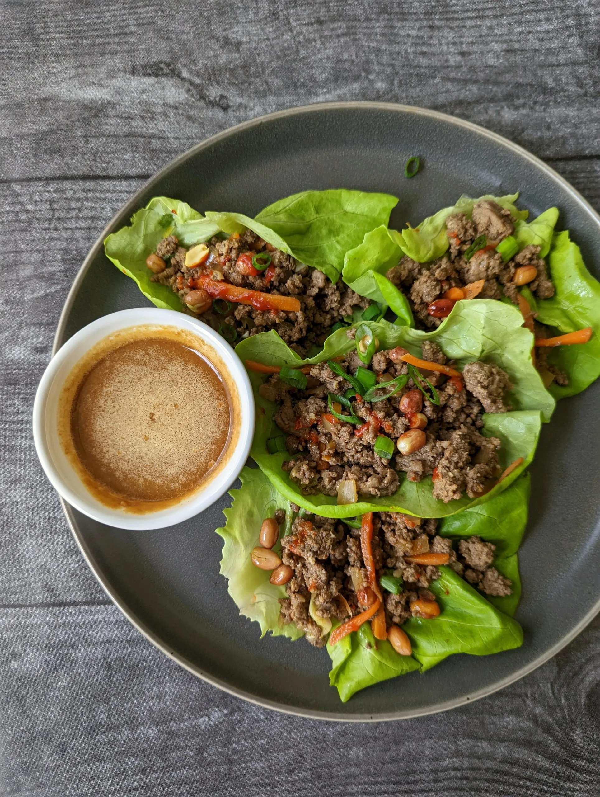 Beef lettuce wraps garnished with scallions, peanuts, and Sriracha.