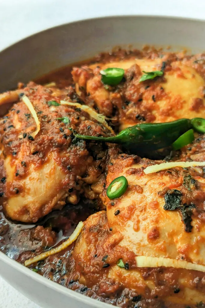 A plate of chicken karahi topped with ginger and green chilies.