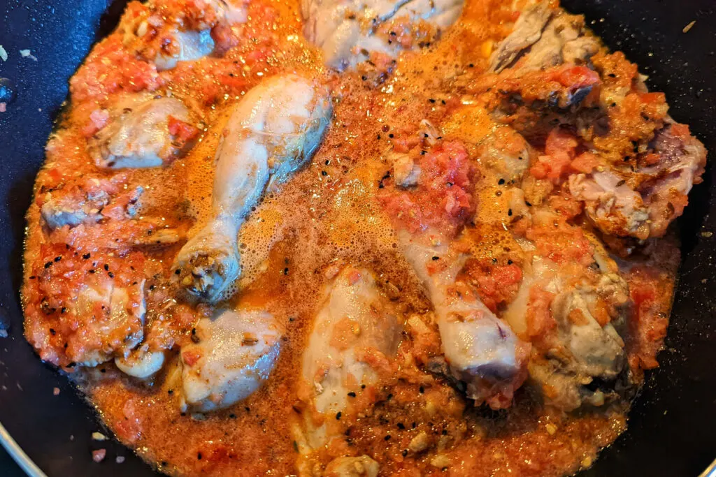 Tomatoes simmering with the chicken in a pan.