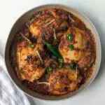 A plate of chicken karahi topped with ginger and green chilies.
