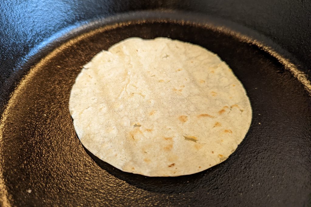Warm the corn tortilla in a cast-iron skillet for 15-30 seconds.