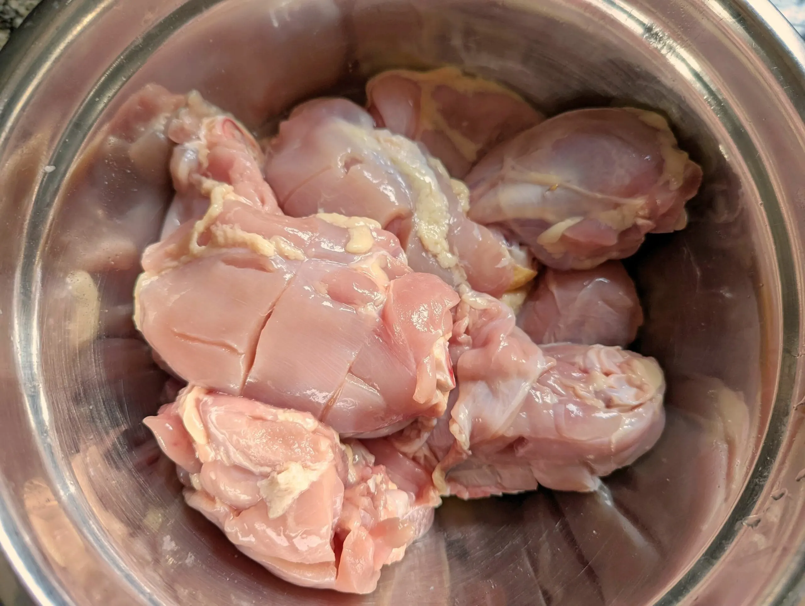 Chicken with slits in a mixing bowl.
