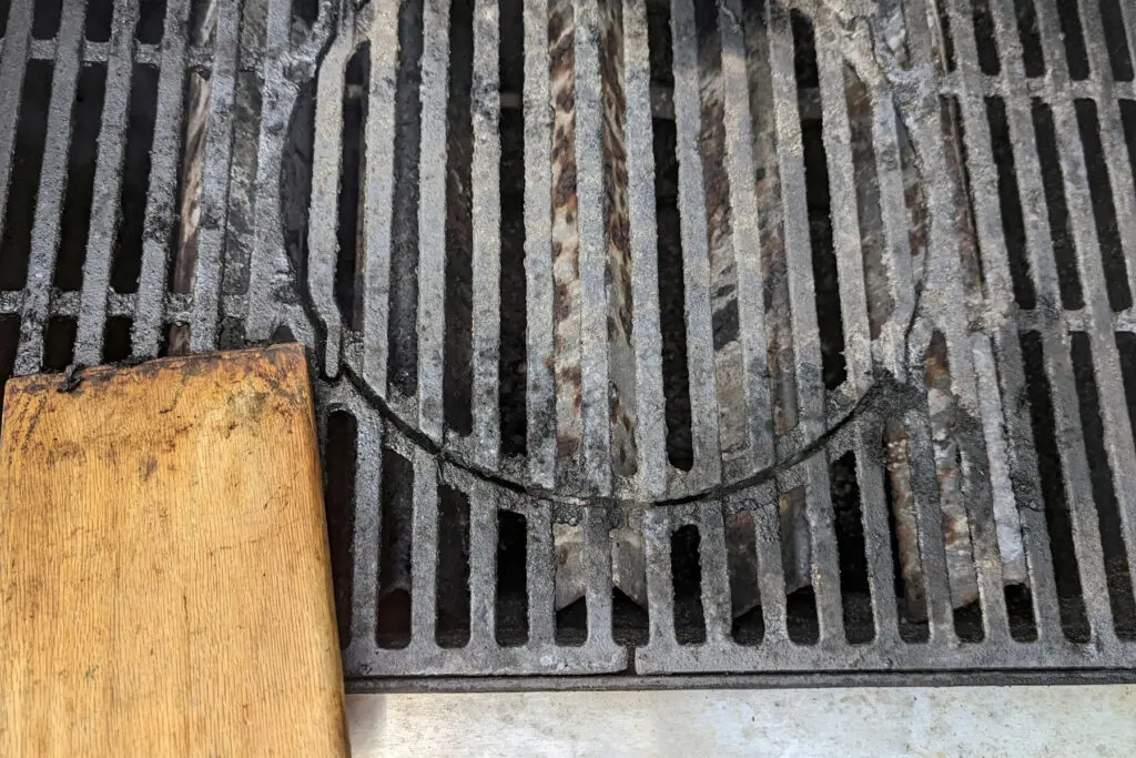 Grill grates being cleaned with a paddle.