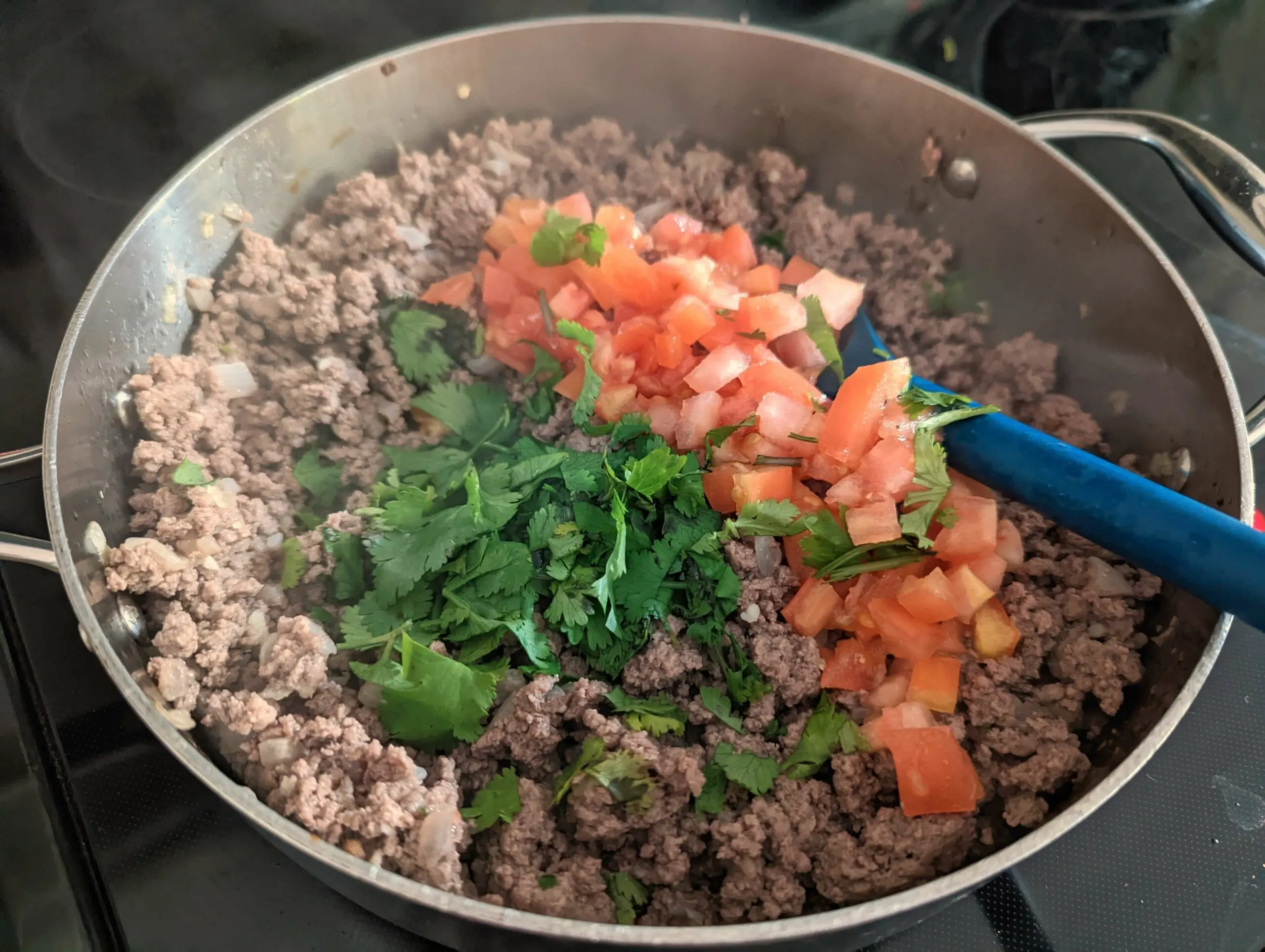 Tomatoes and cilantro are added to the ground beef.