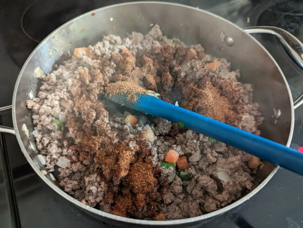 Seasonings top the ground beef mixture in a pan.