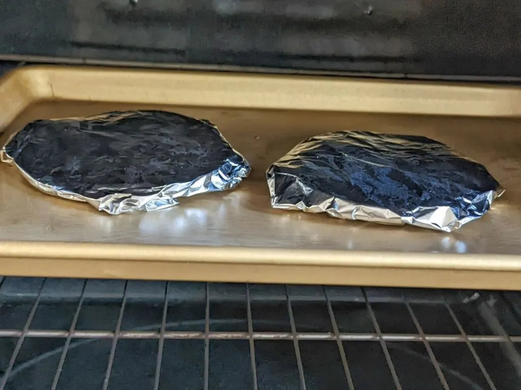 Corn tortillas wrapped in foil on a baking sheet in the oven.
