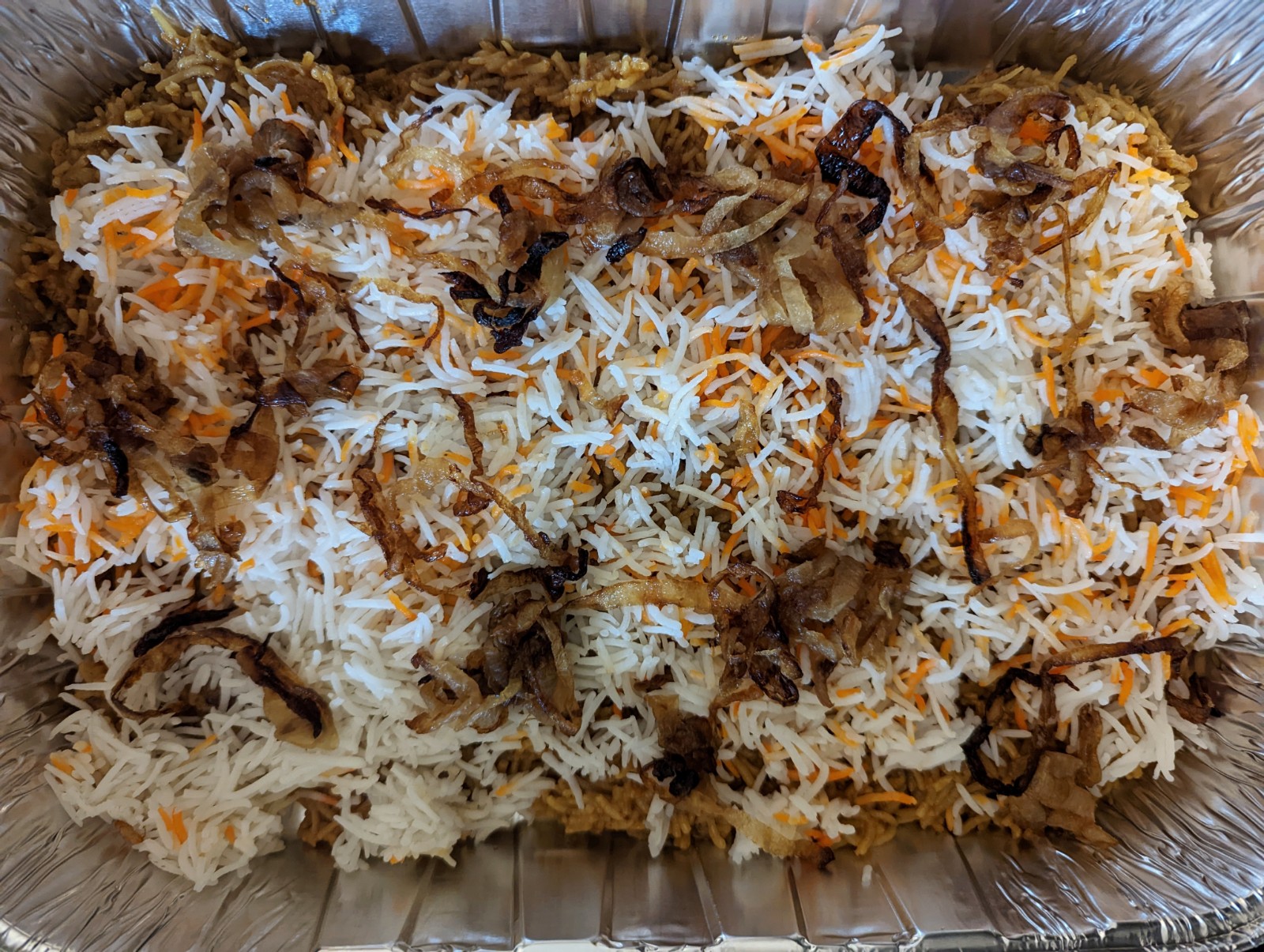 White rice and onions over the biryani rice in a serving dish.