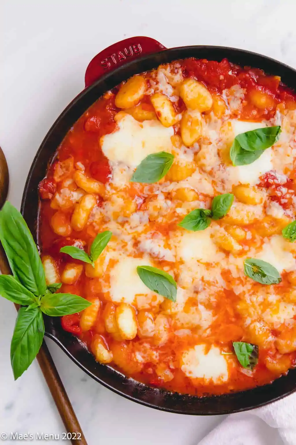 Gnocchi al forno in a skillet surrounded by fresh basil.