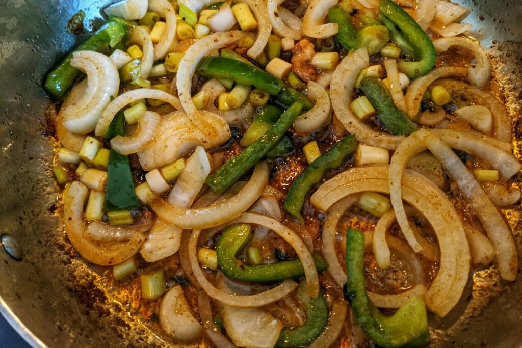 Onions, scallions, and bell peppers cooking in a saute pan.