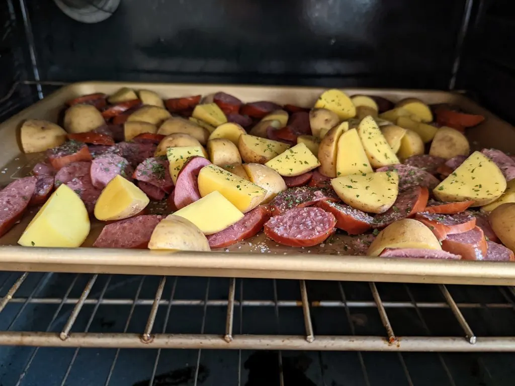 Kielbasa and potatoes on a rimmed baking sheet in the oven.