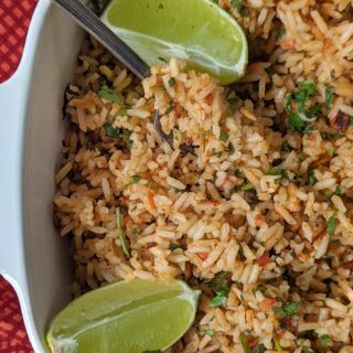 Mexican rice in a serving dish garnished with lime wedges.