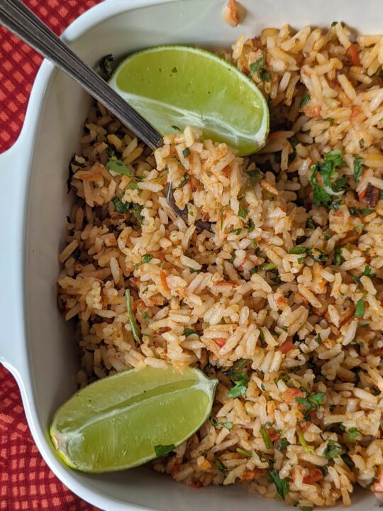 Vegan Mexican rice in a serving dish garnished with lime wedges.