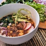A single serving of pozole rojo garnished with fresh cilantro, onion, cabbage, and radish.