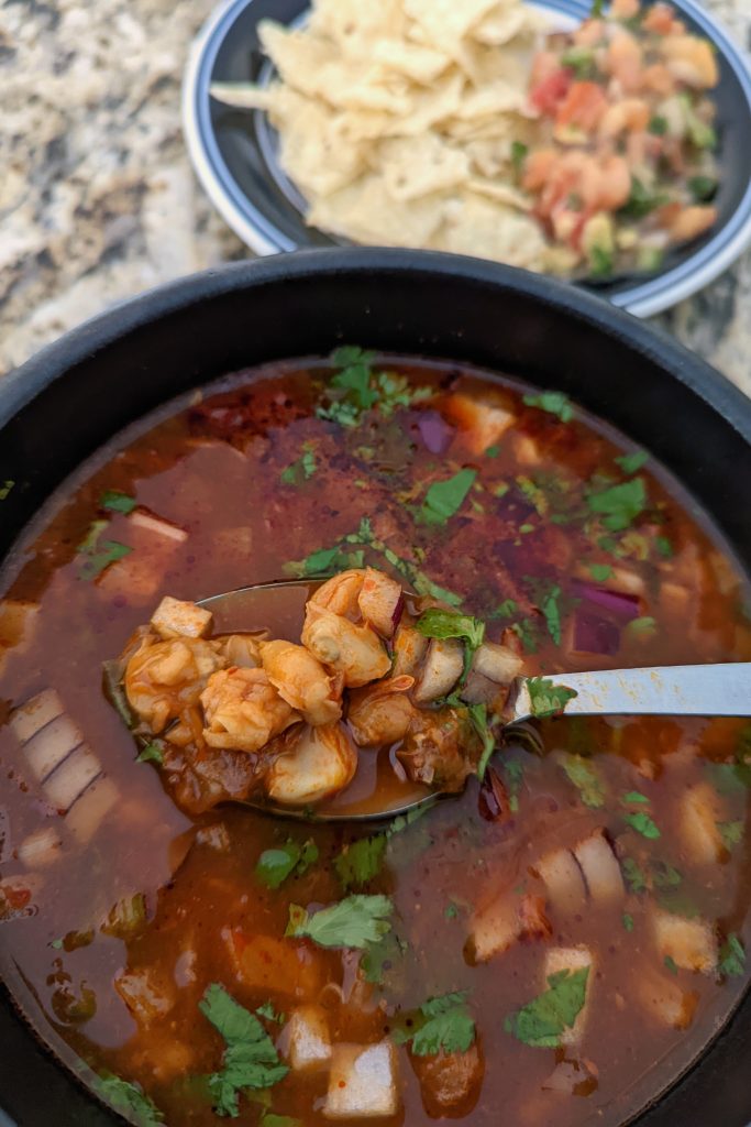 A single serving of pozole rojo garnished with fresh cilantro and red onion.