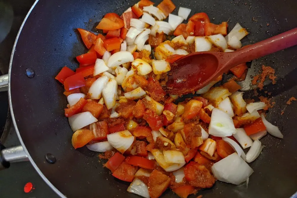 Onions and bell peppers cooking with the curry paste in a pan.