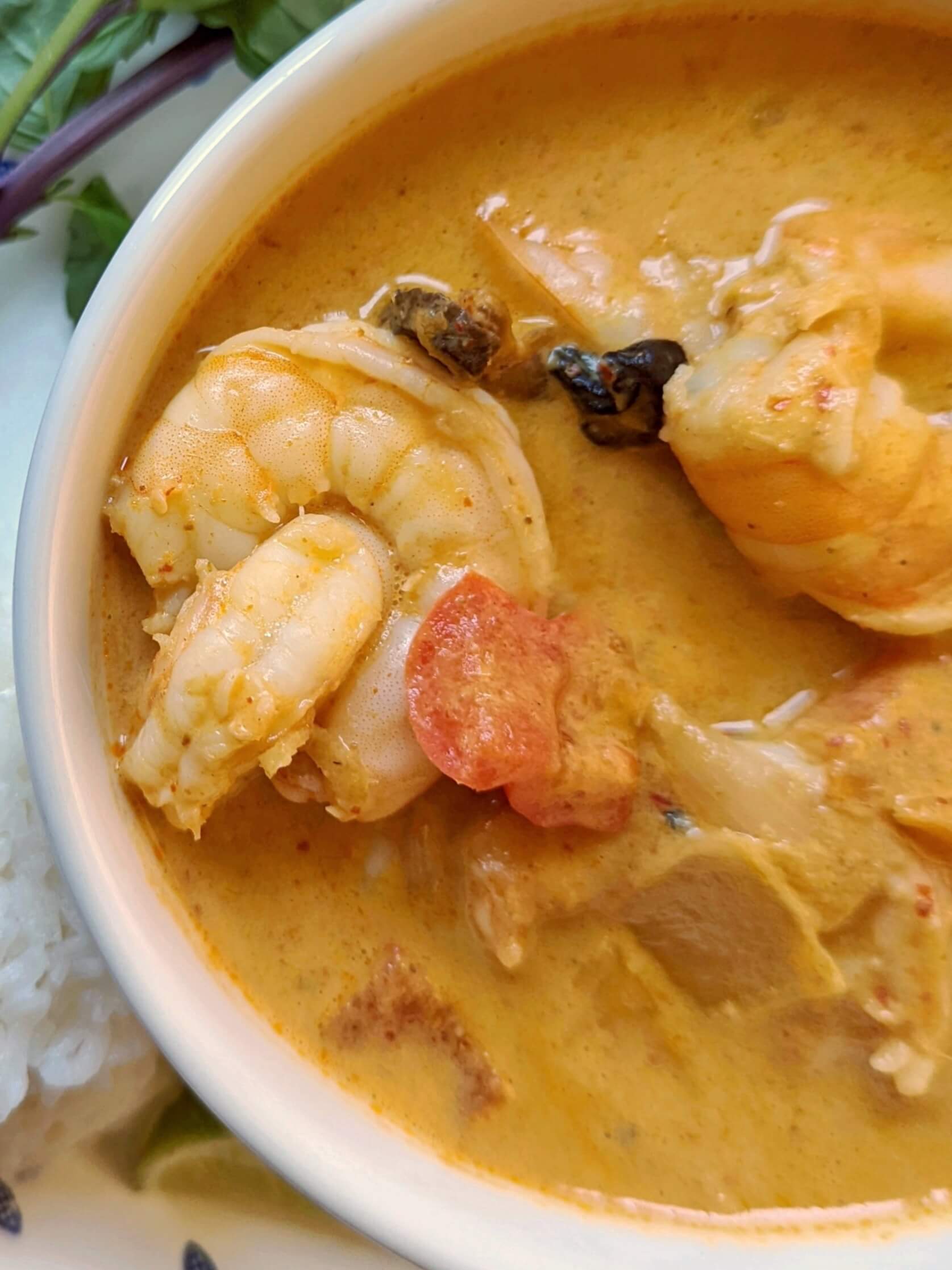 A close up of a small bowl of shrimp panang curry with basil leaves in the background. 
