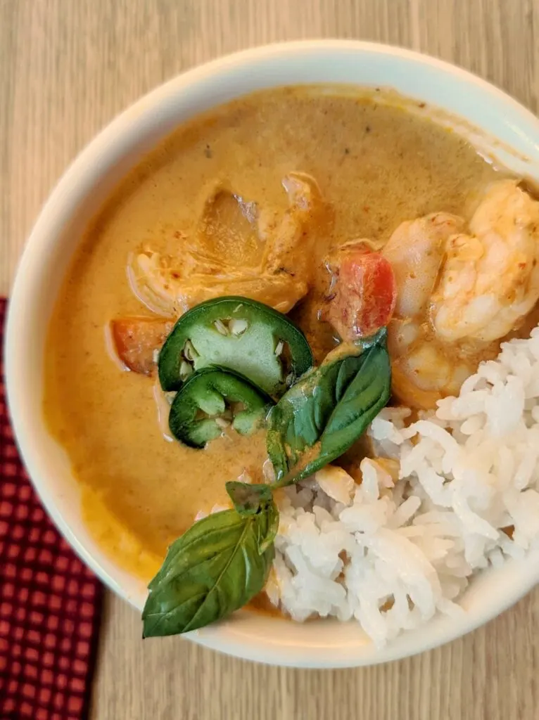 Shrimp panang curry in a small bowl with basil and chilies.