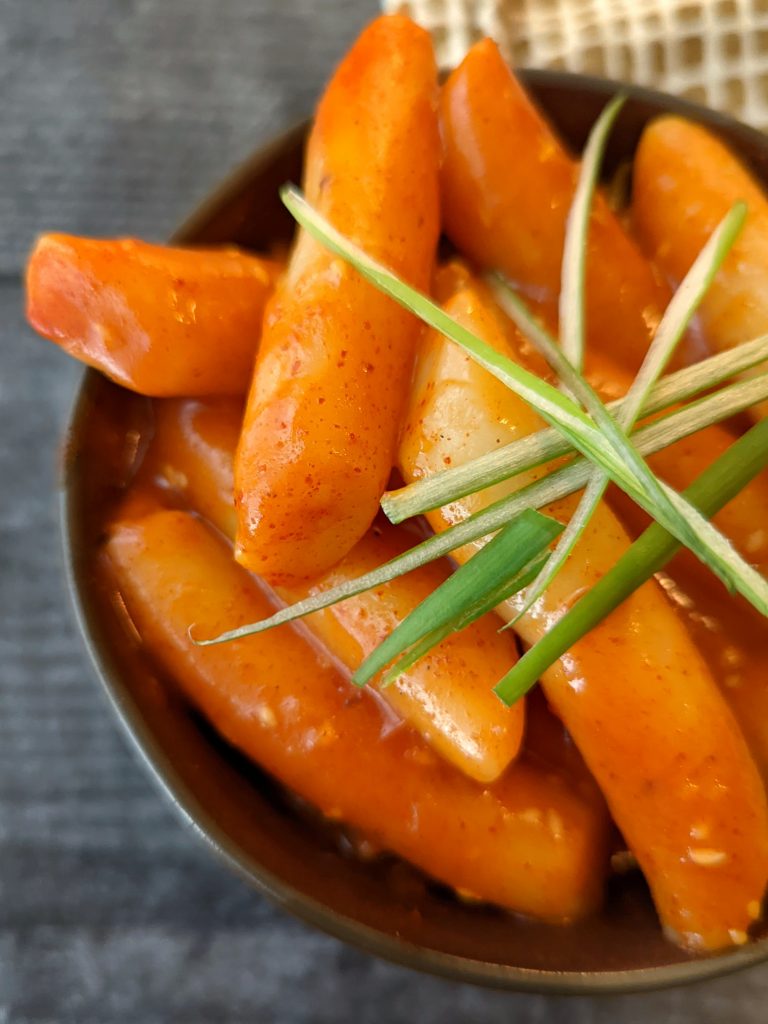 A small bowl of tteokbokki garnished with scallions and ready to serve.