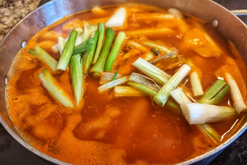 Scallion whites and rice cakes are added to the broth to finish the tteokbokki.