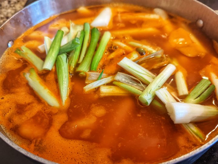 Scallion whites and rice cakes are added to the broth to finish the tteokbokki.
