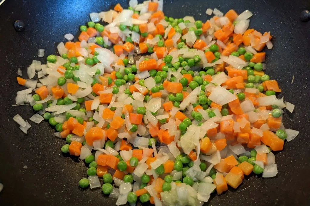 Frozen peas, carrots, and onions cooking in a wok.