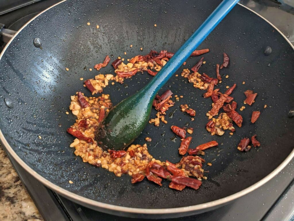 Bean paste, garlic, ginger, and chilies frying in a wok.